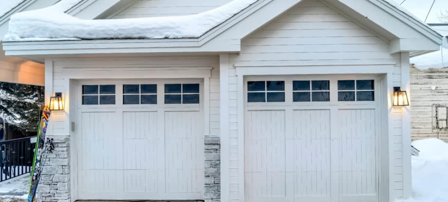 A mountain home with two wooden garage doors with a pair of skis leaning on the wall.