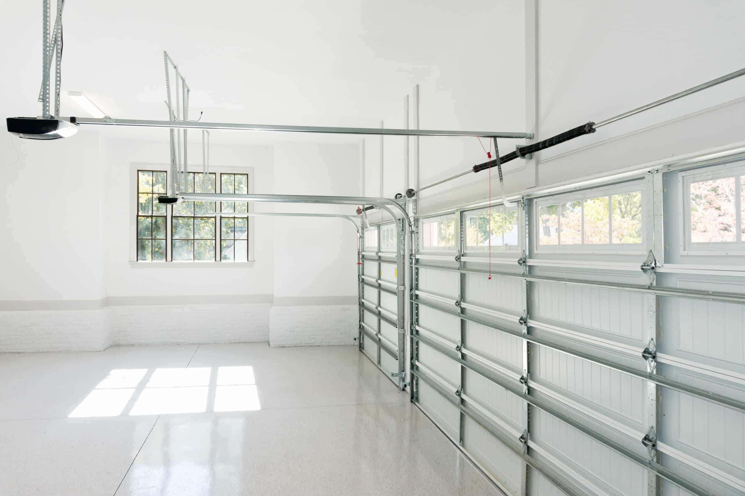 Two garage doors with overhead openers in a clean, white garage.